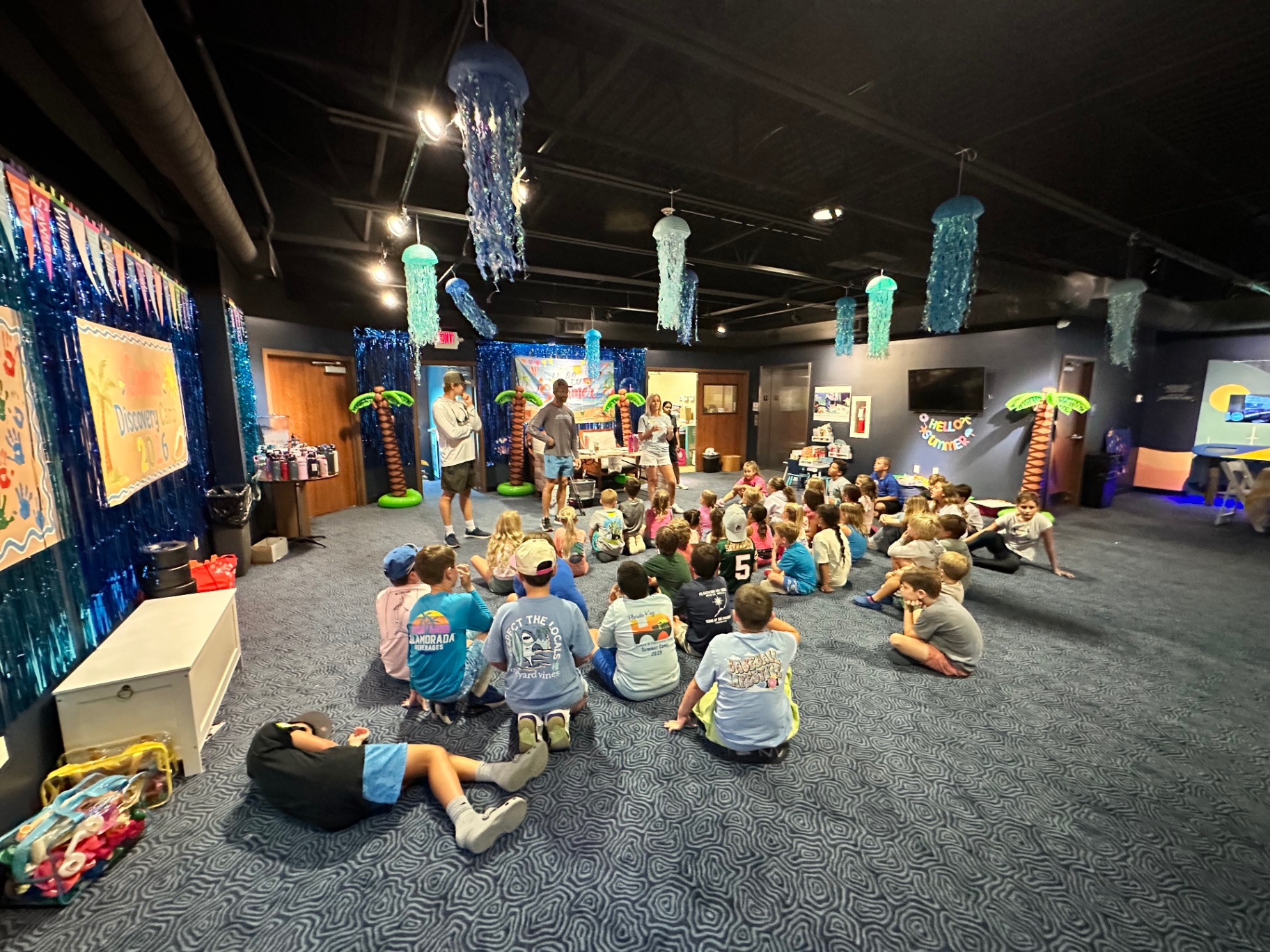 Campers gathered on the floor for a group session beneath hanging jellyfish decorations