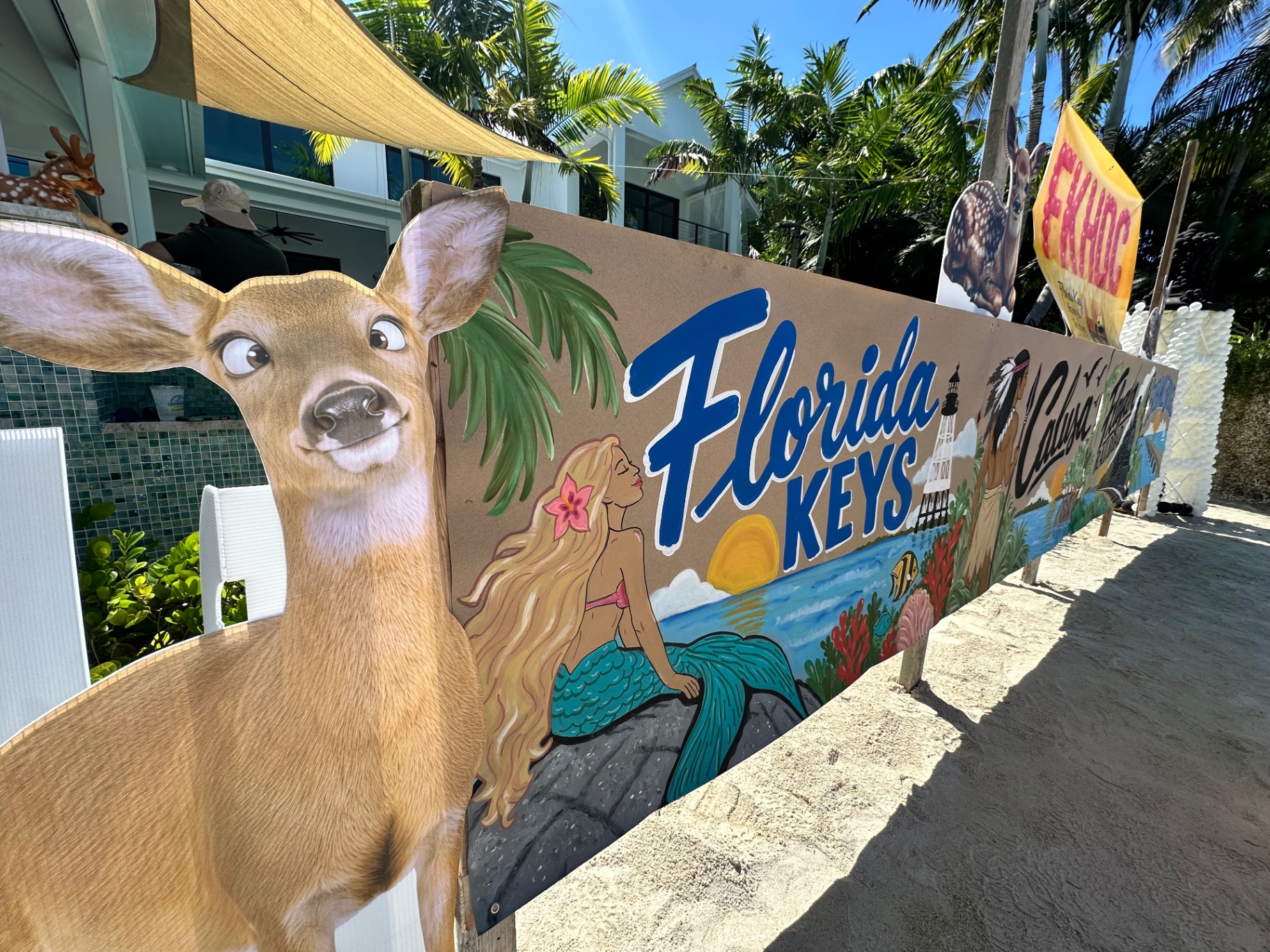 A cutout of a Key deer beside a hand-painted Florida Keys scene with the Discovery Center's flag flying above it at the Conch Scramble