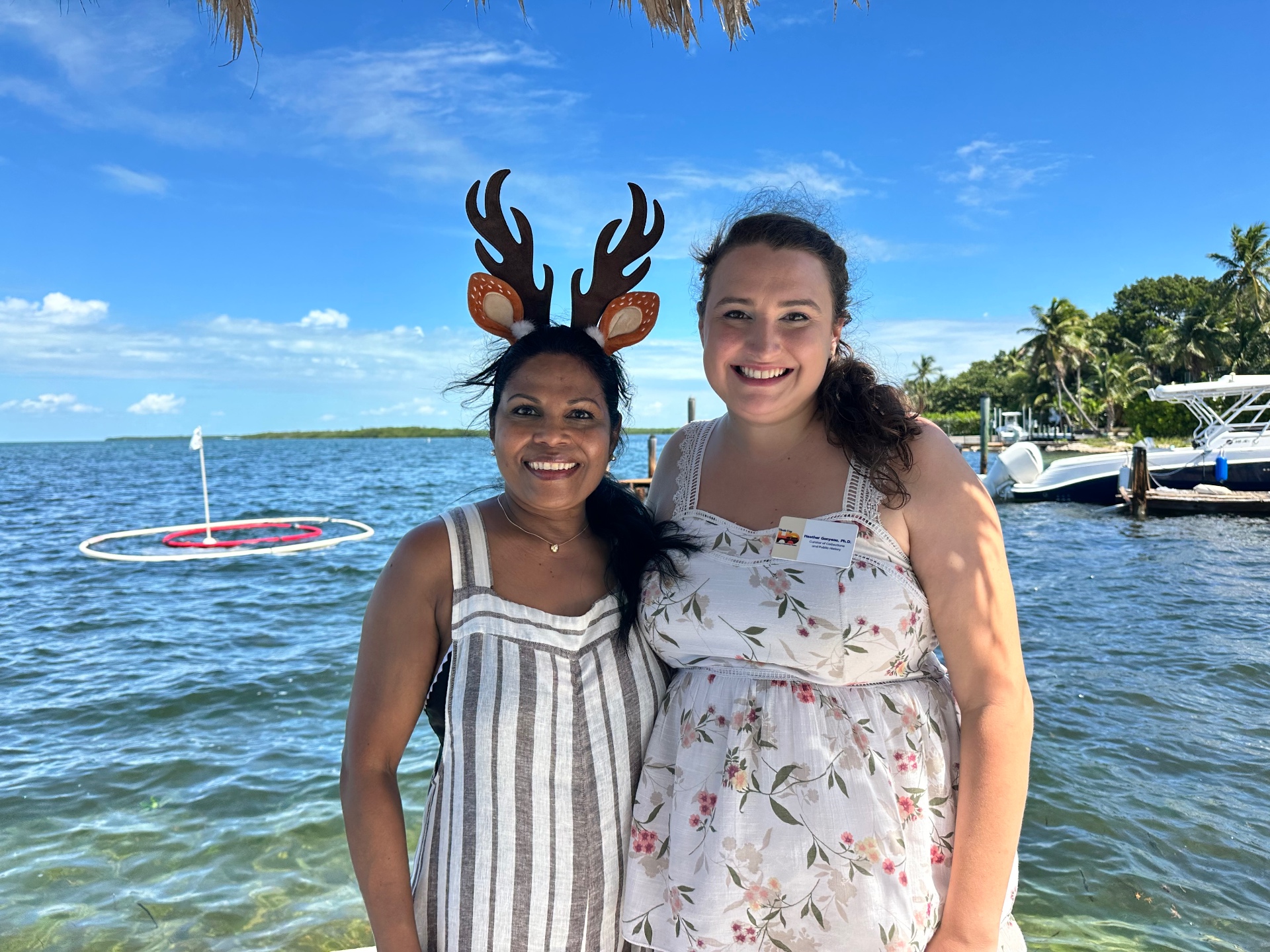 Two staff members in deer-ear headbands pose by the water at the Center's Conch Scramble hole