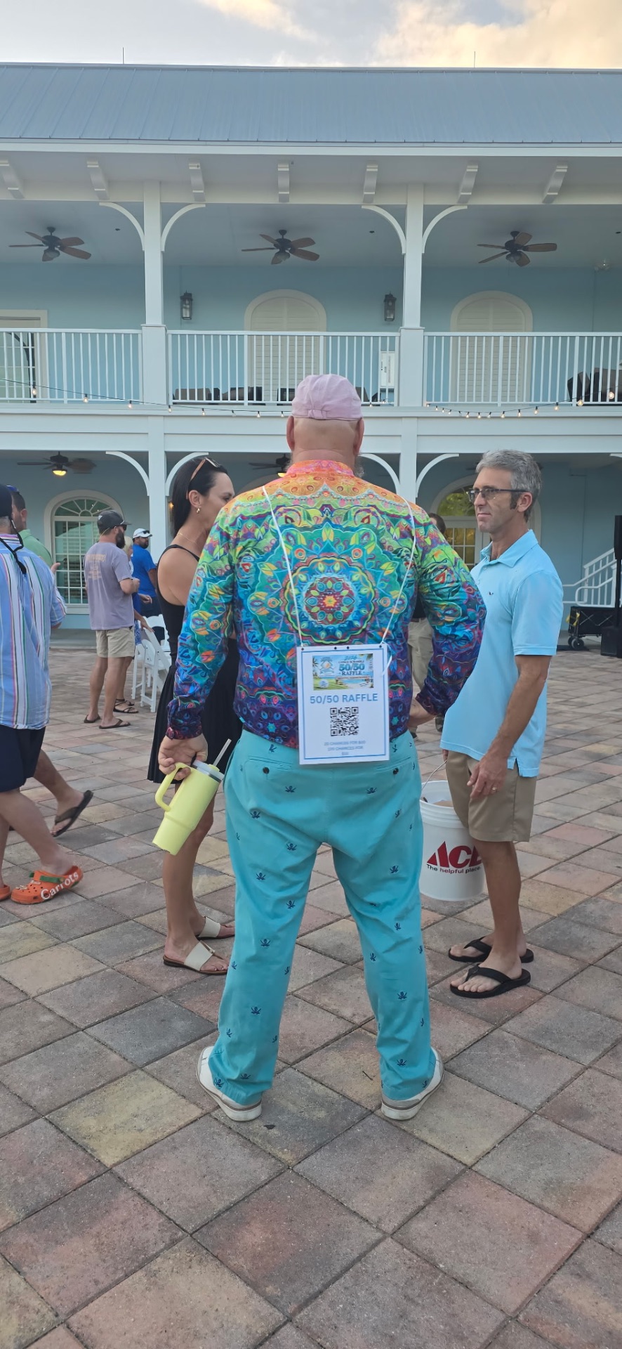 A volunteer in a colorful shirt wears the 50/50 raffle sign on his back at the Conch Scramble kickoff party