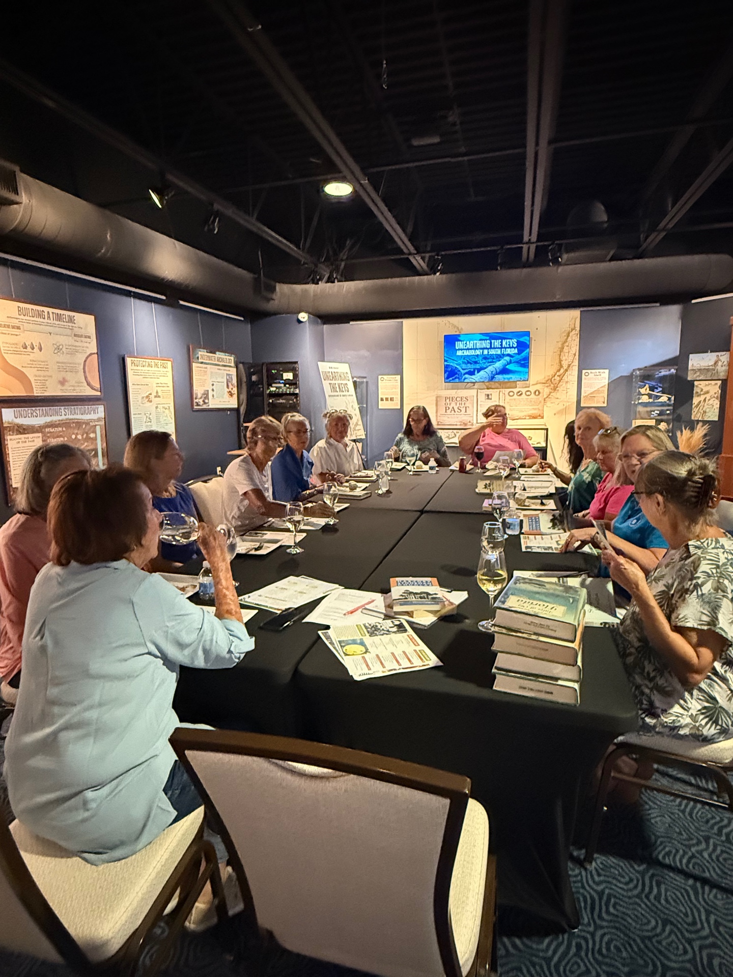 Book club members gathered around the table in the Unearthing the Keys gallery, with stacks of books and refreshments