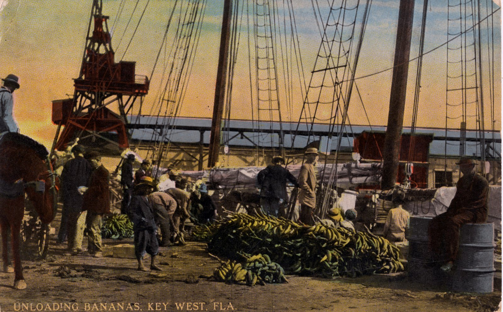 Dock laborers unloading bunches of green bananas onto a Key West wharf beside a masted sailing ship
