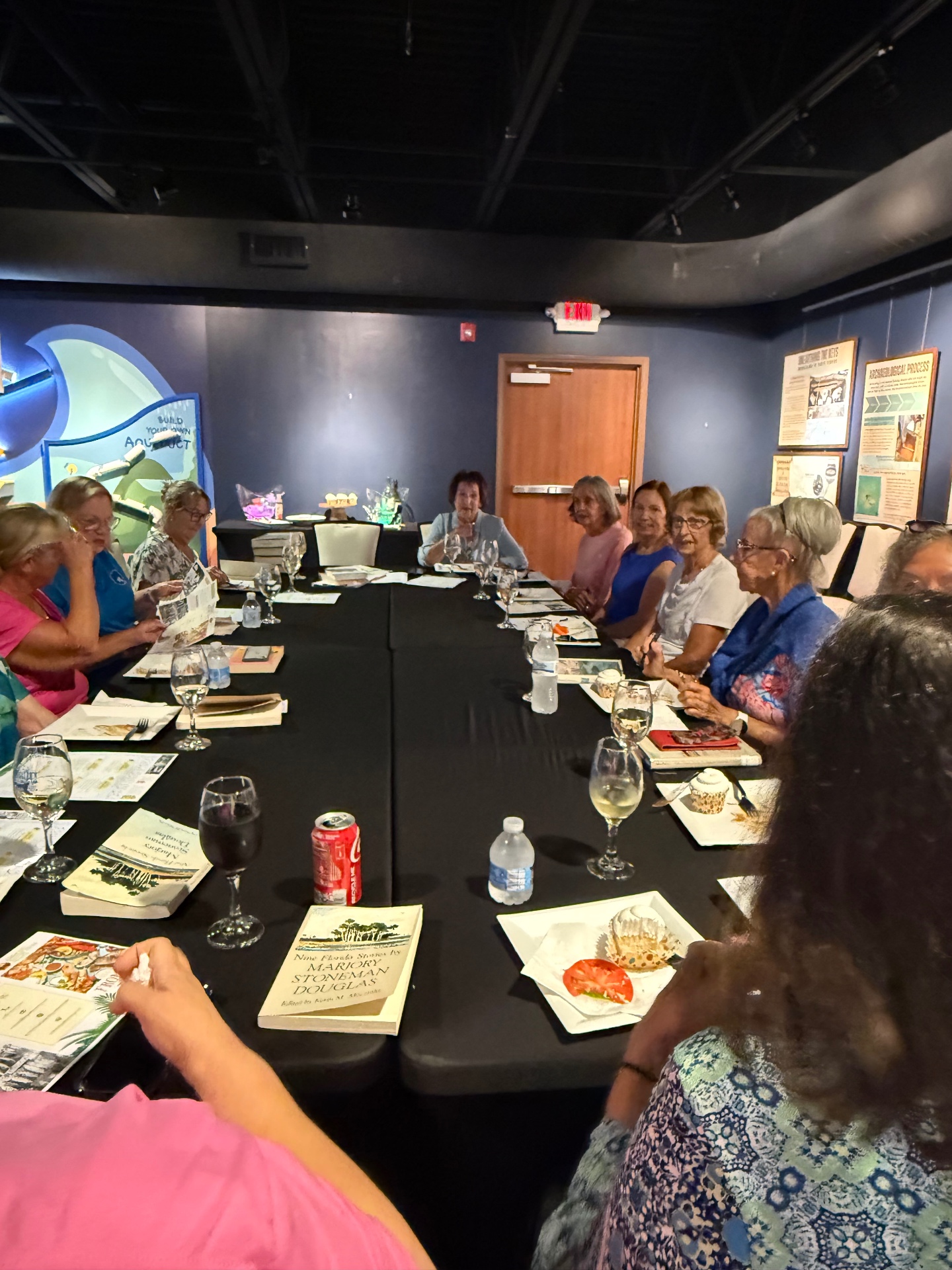 Book club conversation around a long table, with copies of Nine Florida Stories by Marjory Stoneman Douglas