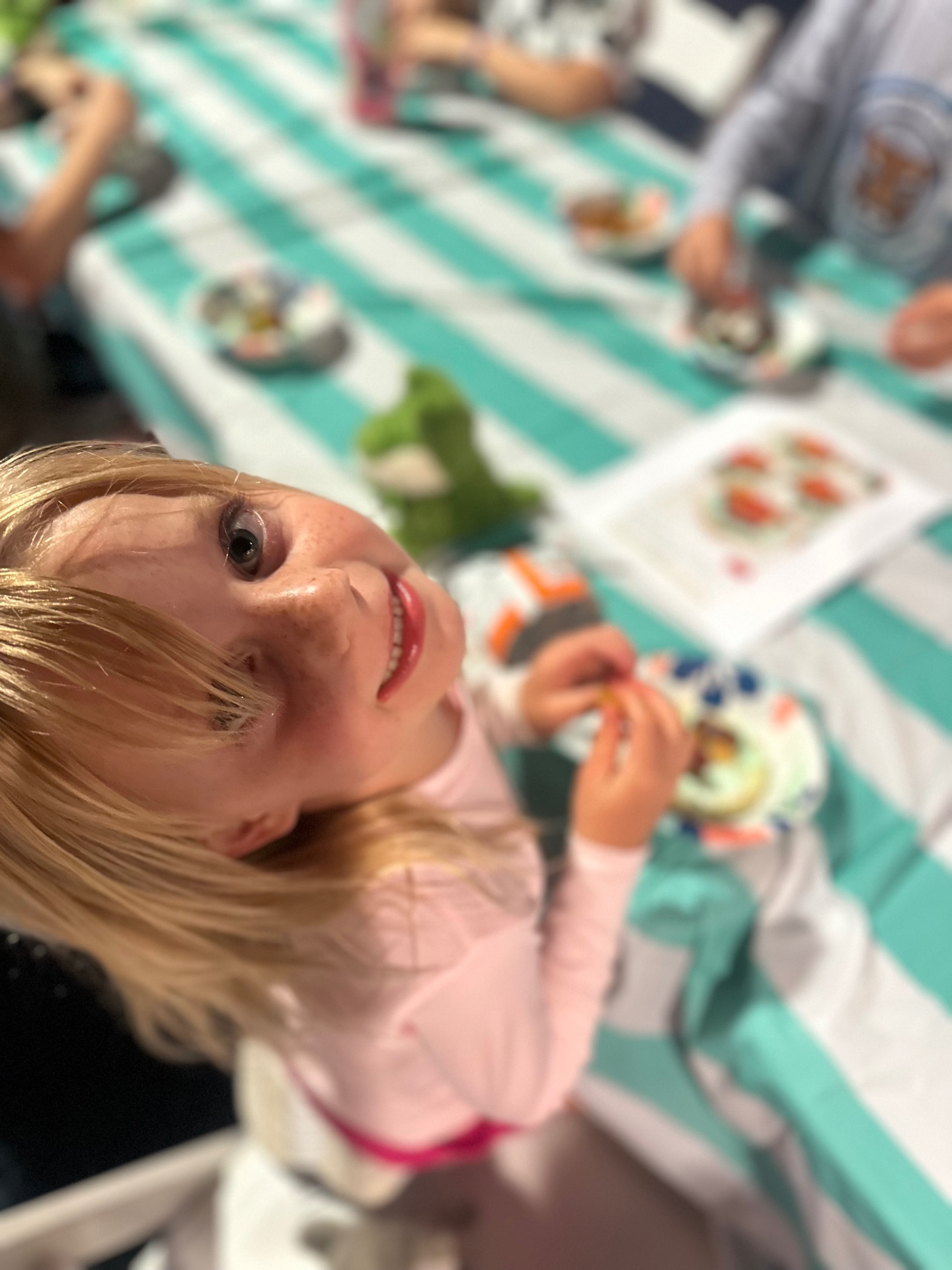 A young girl at a group table looks up from her activity and smiles warmly at the camera.