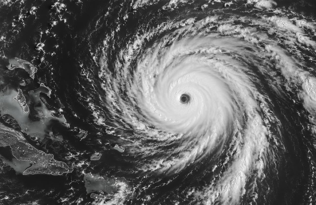 Black and white satellite view of a powerful hurricane with a clearly defined eye spiraling over the ocean, islands visible along the edge of the frame