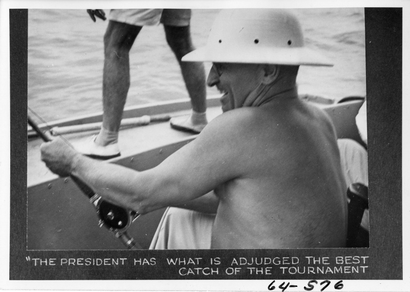 President Harry Truman, shirtless in a pith helmet, laughing as he works a rod and reel in a small boat off Key West